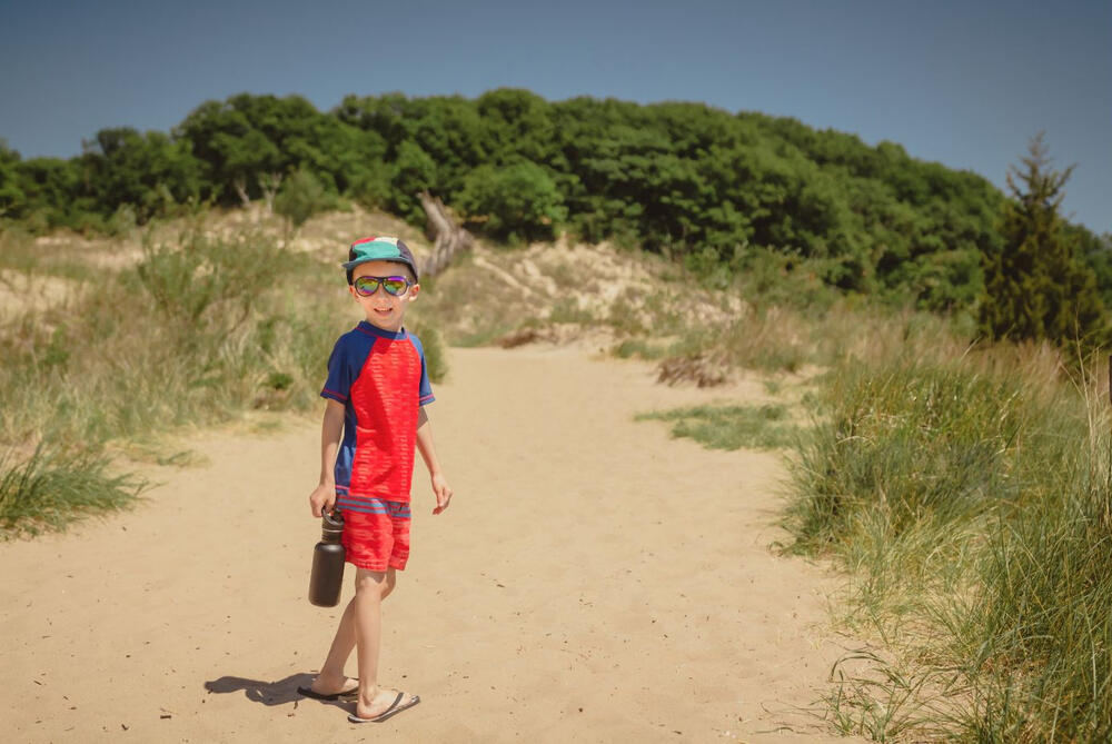 A young boy comes prepared for a day of hiking in Indiana Dunes with a water canteen, a hat, and sunglasses