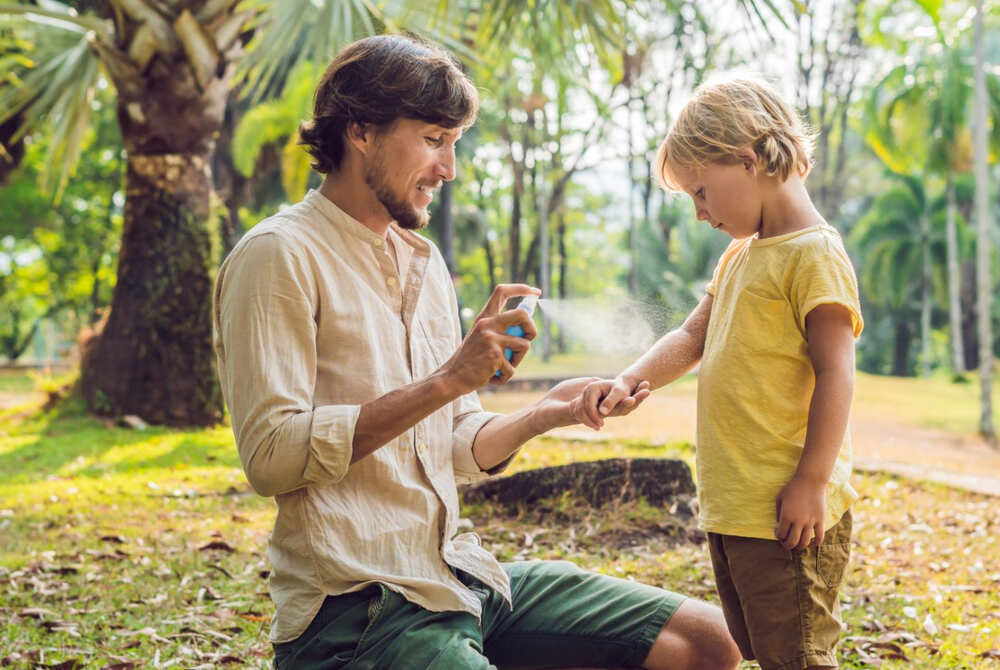 adult spraying insect repellent on a child to protect from bug bites in the parks