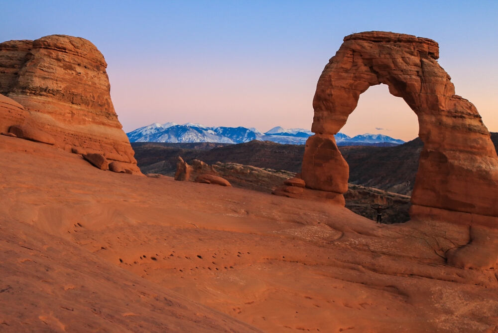Delicate Arch at sunset with snow capped mountains in background