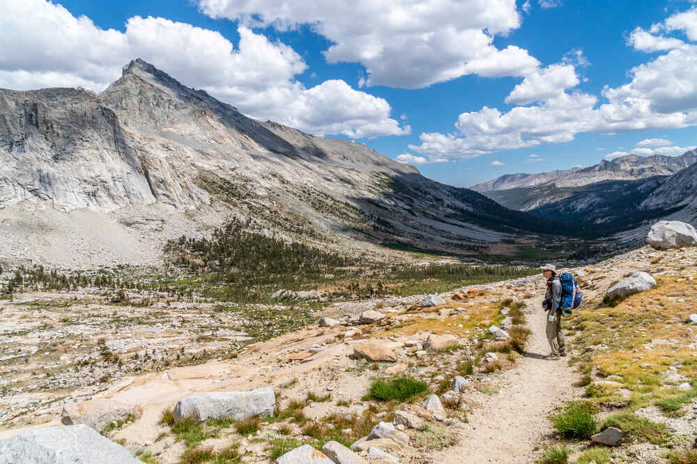 A backpacker hiking along the High Sierra Trail stopping to admire the view of rugged mountains and valleys on a beautiful spring day