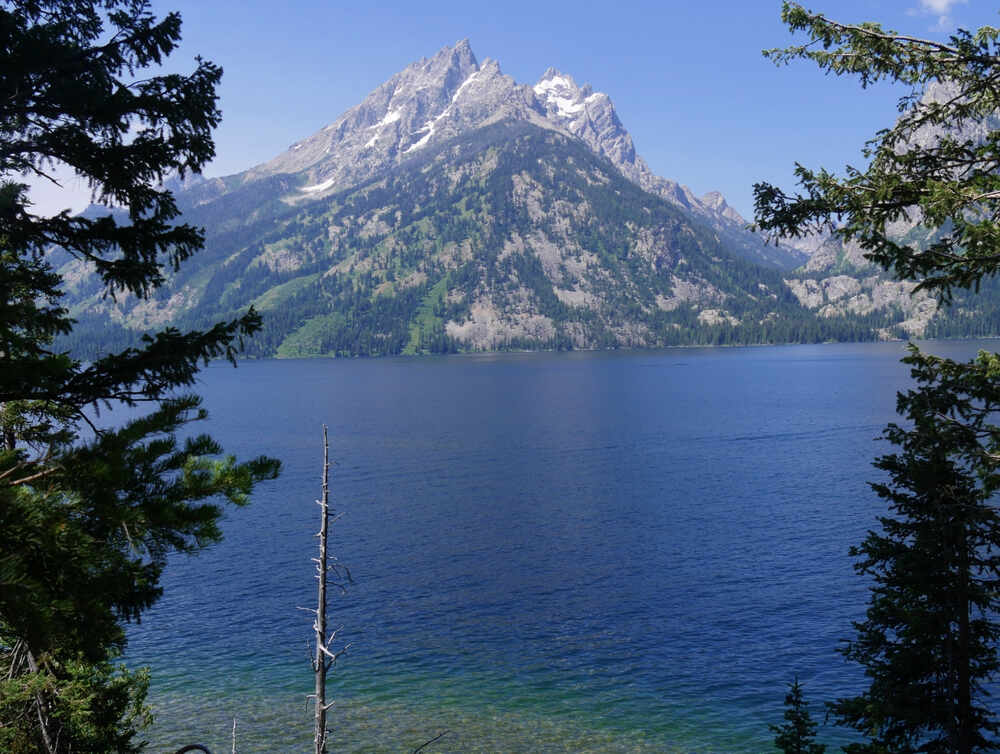 pristine water at Jenny Lake, reflecting the surrounding peaks of the Teton Range with shades of deep blue and turquoise near the shoreline